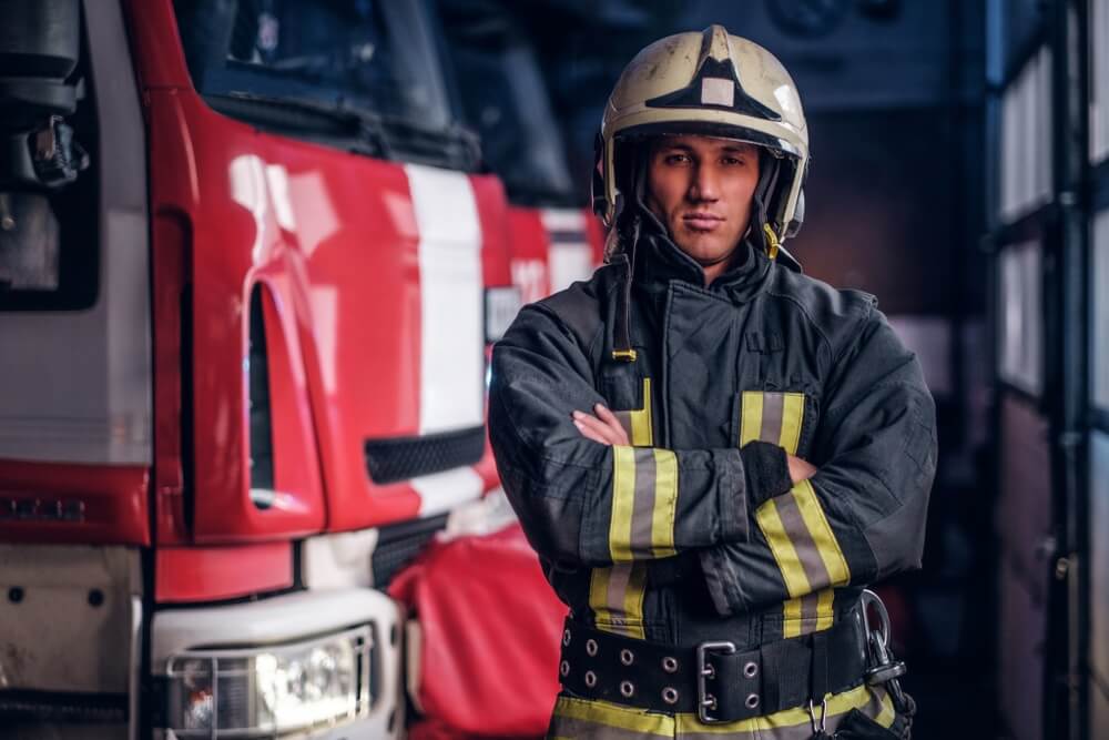 fireman wearing protective uniform standing next to a fire engine in a garage of a fire department