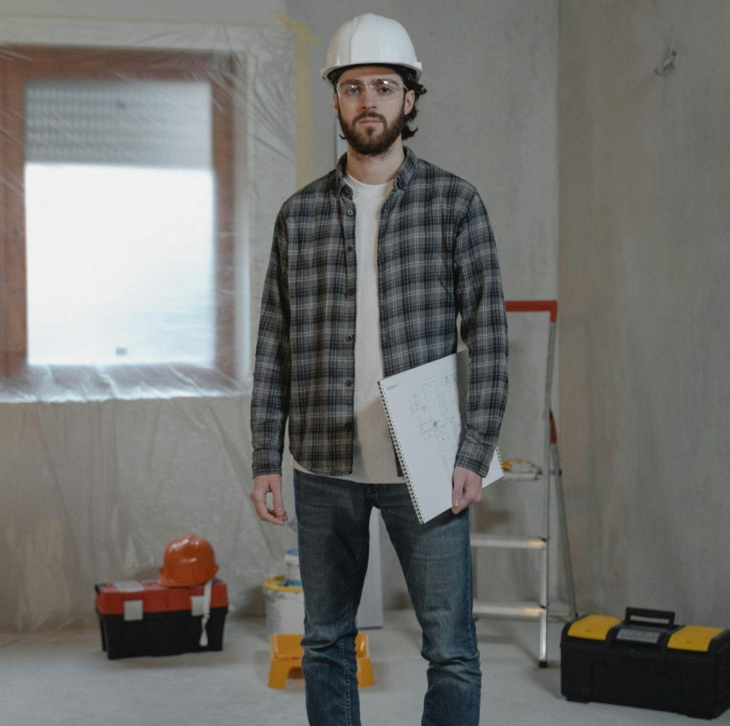 Man in jean and a plaid shirt standing in a room that is under construction